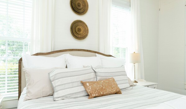 Una cama bien tendida con ropa de cama a rayas y una almohada decorativa, un cabecero de madera y dos elementos decorativos en la pared.