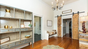 Una habitación con piso de madera, un candelabro, un banco y una puerta con un letrero de 'Welcome'.