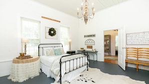 Un dormitorio con cama, candelabro, escritorio y puerta que da a otra habitación.