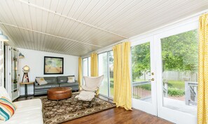 Una sala de estar acogedora con un sofá gris, un tapete estampado y un reposapiés marrón.
