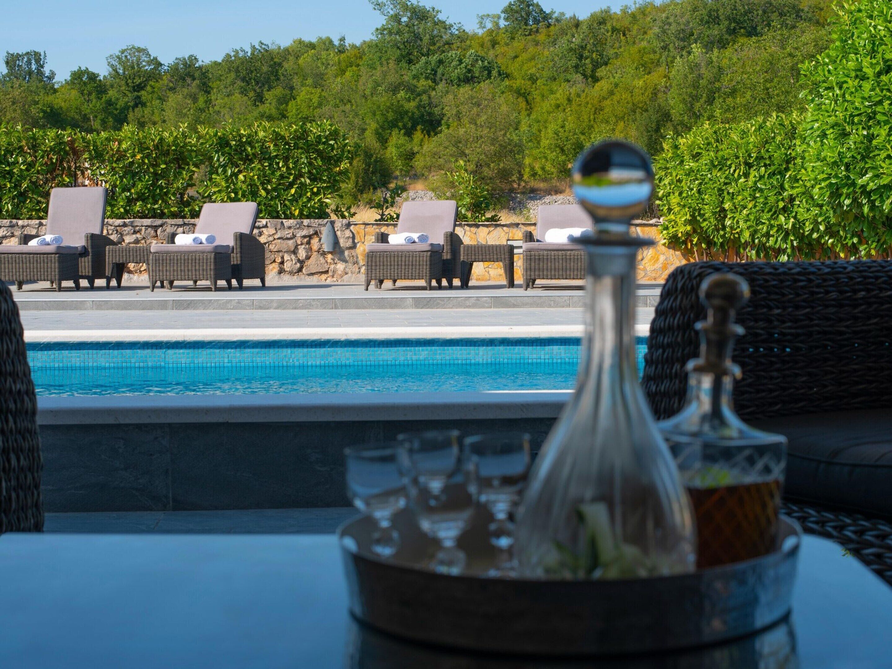 A poolside area with wicker lounge chairs and a table with a glass decanter and glasses.