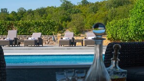 Un espace aménagé au bord de la piscine, avec des fauteuils de relaxation en osier et une table sur laquelle se trouvent une carafe en verre et des verres.