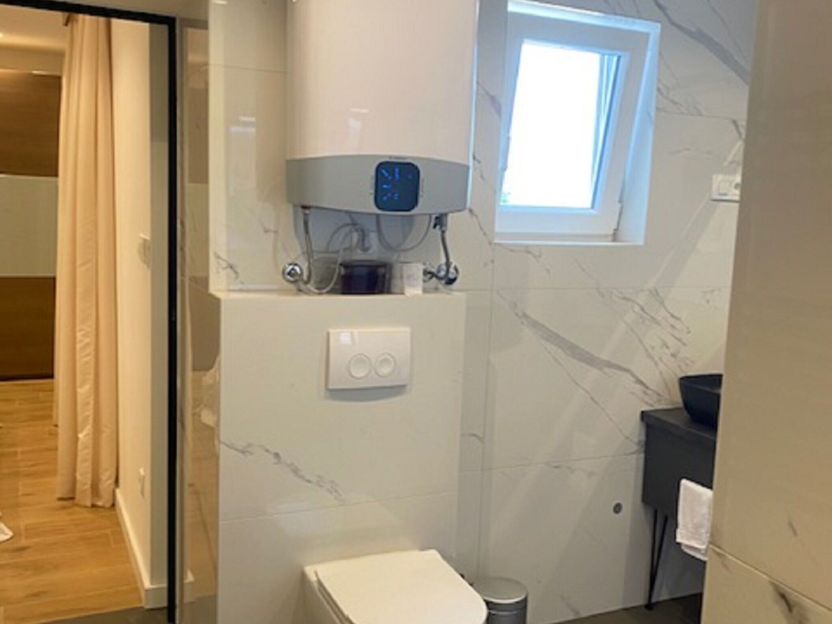 A modern bathroom with a toilet, a small window, a towel rack, and a marble wall.