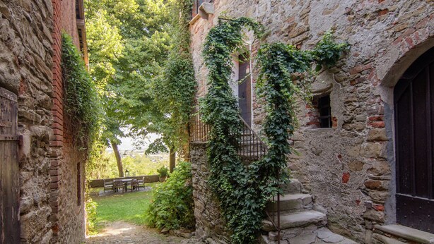 Un carreró empedrat amb parets de pedra, una porta de fusta i una escala que mena a un segon pis.