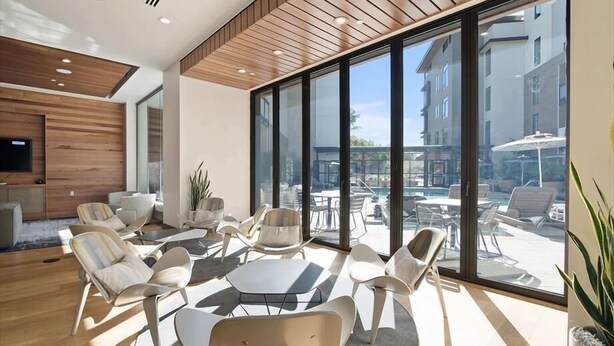 A modern lounge area with a large glass wall, wooden ceiling, and contemporary furniture.
