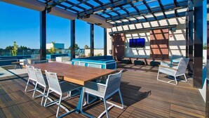 An outdoor deck with a wooden table and chairs, a blue sofa, and a TV screen.