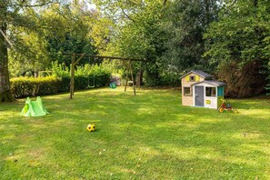 Een gazon met een speeltuintje, een schommel en een groene tent.