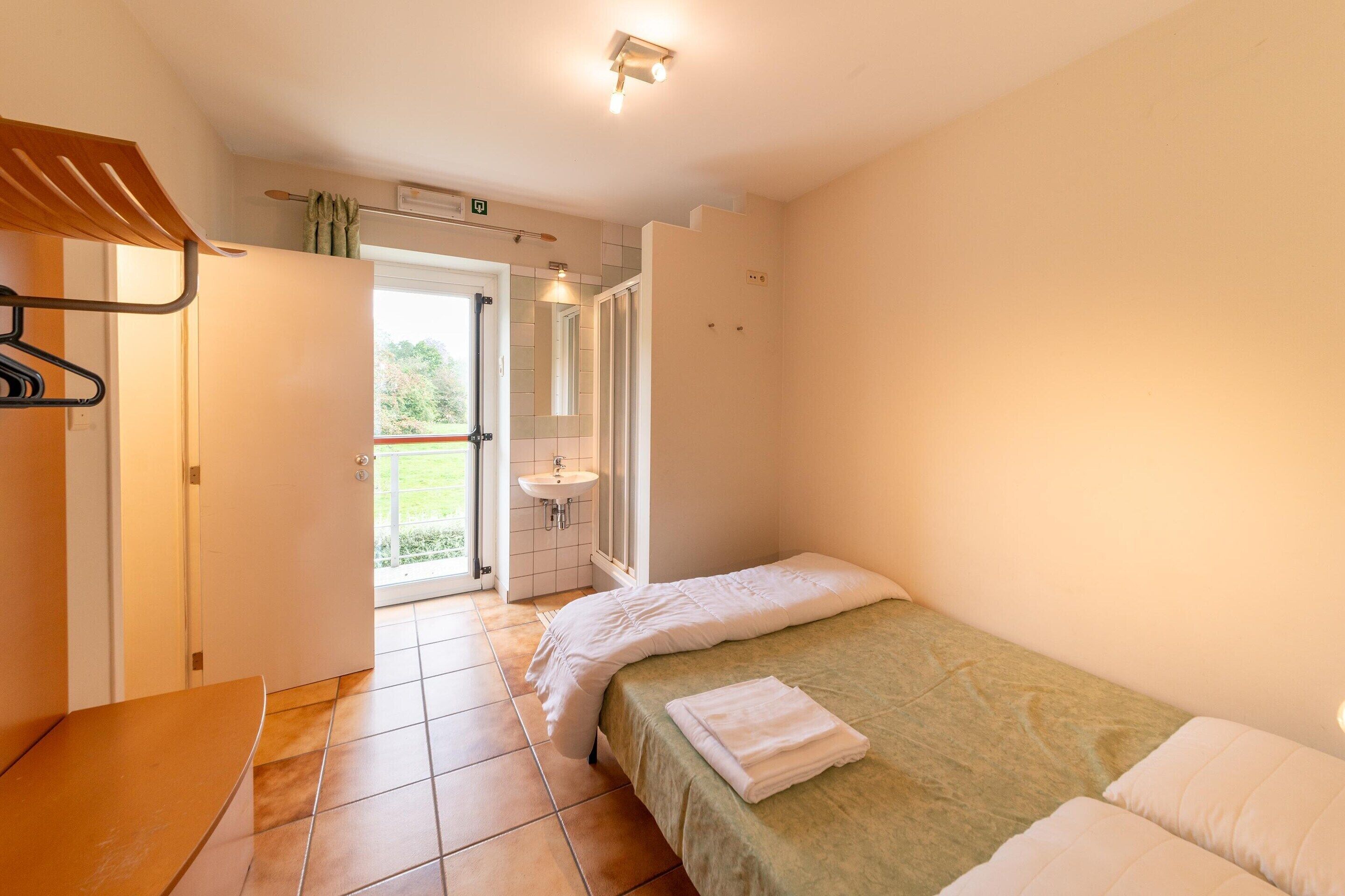 A bedroom with a bed, a bench, a sink, and a door leading to a balcony.
