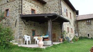 Un edificio in pietra con un portico coperto, posti a sedere all'aperto e piante in vaso.