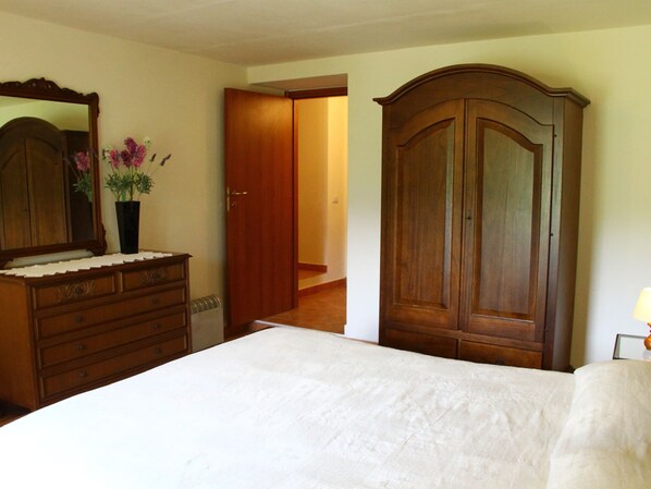 A bedroom with a wooden dresser, a mirror, a bed, and a door leading to another room.