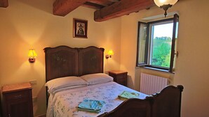 Un dormitorio con una cama de madera, dos mesitas de noche, una lámpara de noche, una ventana con vistas y un plafón.
