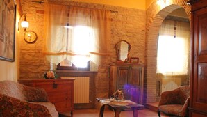 Una habitación acogedora con pared de piedra, una mesa de madera, dos sillones estampados, un aparador y un espejo.