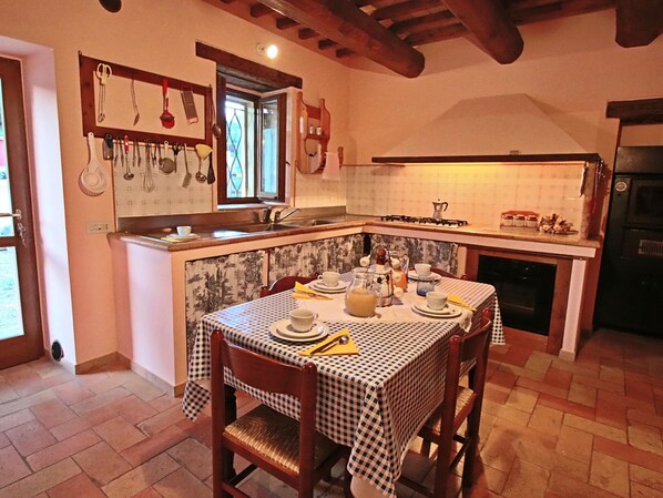 Une cuisine chaleureuse avec une nappe à carreaux, des chaises en bois et une fenêtre.