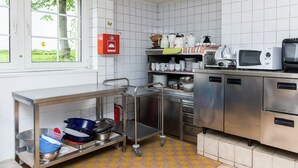 Een keuken met roestvrijstalen apparatuur, een raam met uitzicht op groen en een brandblusser aan de muur.