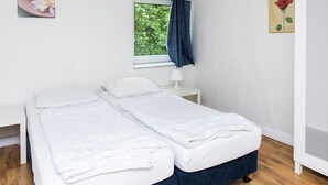 Slaapkamer met twee bedden, een raam met uitzicht op groen, een nachtkastje met een lamp en wanddecoratie.