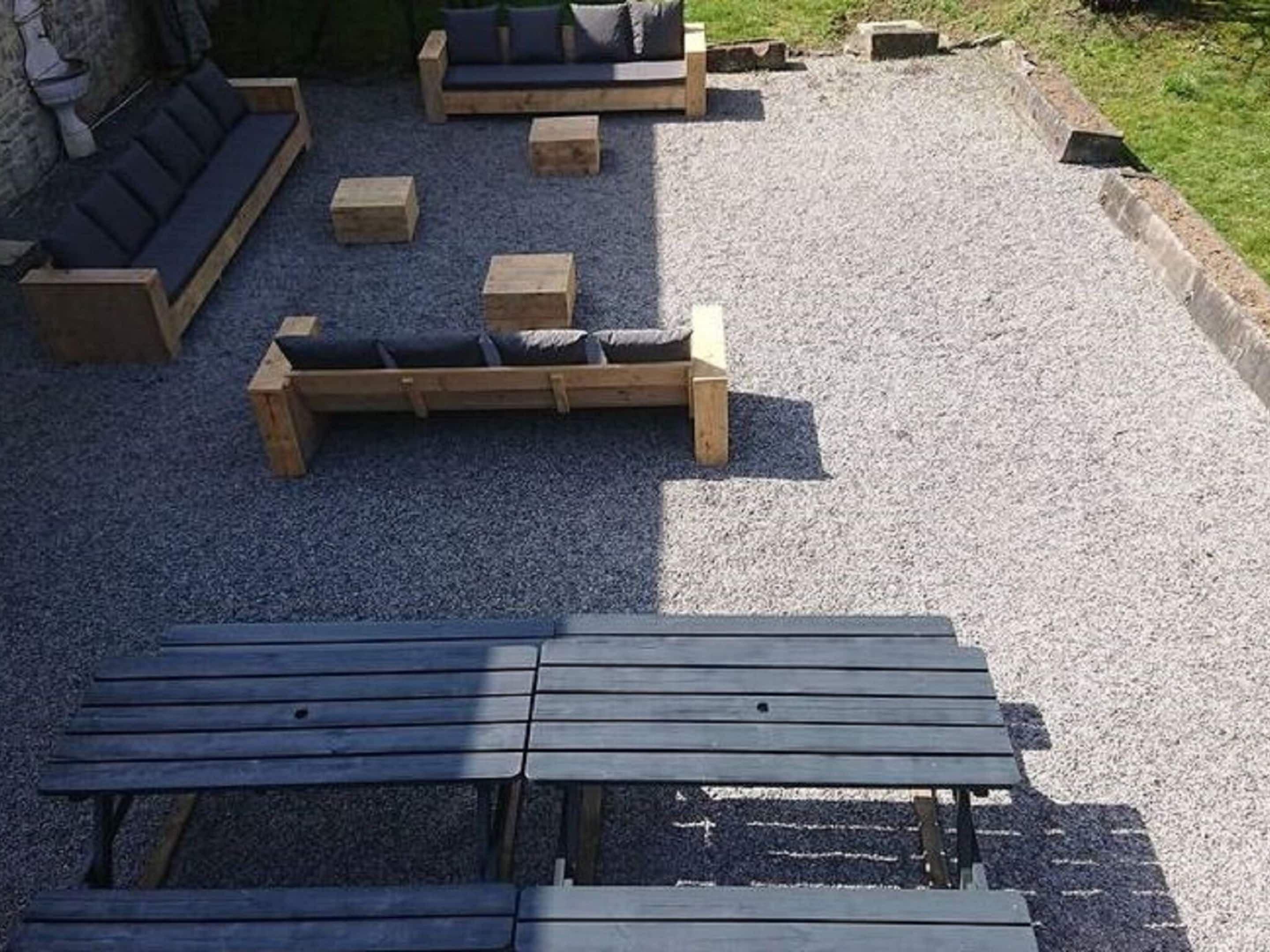 A gravel patio with wooden furniture including a sofa, benches, and a table.