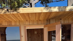 Una sauna de madera con vista a la playa, bancos de madera y una puerta de vidrio.
