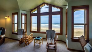 Una habitación con ventanas amplias que dan a una playa, muebles de madera y una lámpara.