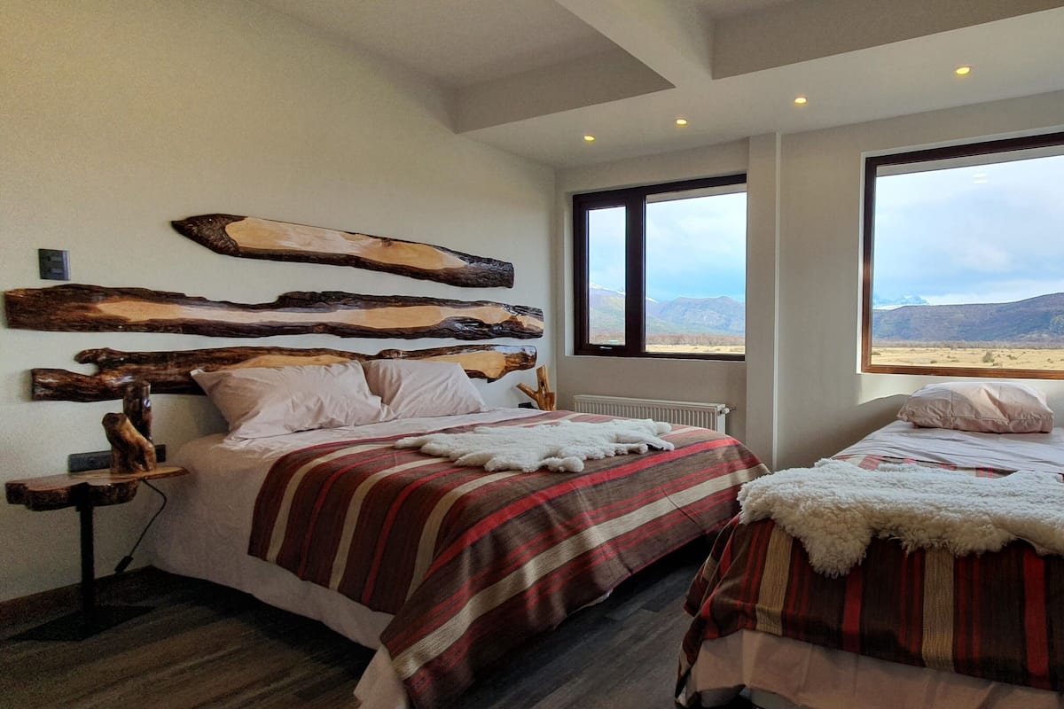 Ein Schlafzimmer mit zwei Betten, einem großen Fenster und Blick auf die Berge sowie Holzdekor an der Wand.
