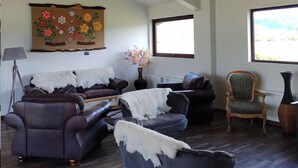 Een ruime woonkamer met donker houten vloeren, leren banken, een groot schilderij en twee ramen die natuurlijk licht binnenlaten.
