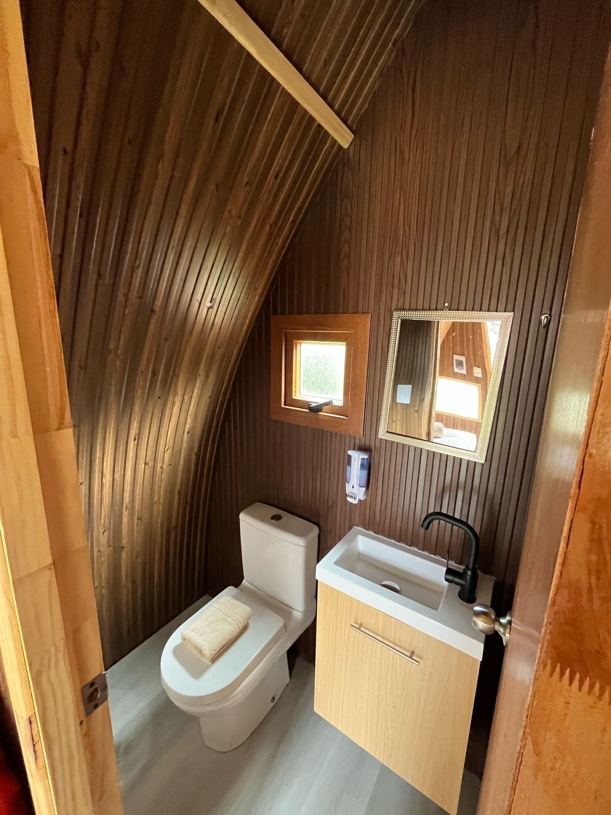 A compact, wooden-paneled bathroom with a toilet, sink, and mirror.