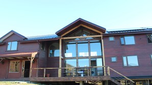 Een houten huis met twee verdiepingen, een balkon en grote ramen.