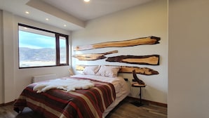 Een slaapkamer met een groot raam, een bed met een gestreept deken en drie houten wanddecoraties.