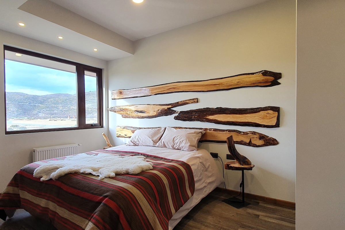 Ein Schlafzimmer mit großem Fenster, einem Bett mit gestreiftem Überwurf und drei hölzernen Wandbildern.