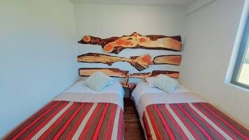 A room with two beds, each with striped bedding, a wooden headboard with a painted design, and a window on the right.
