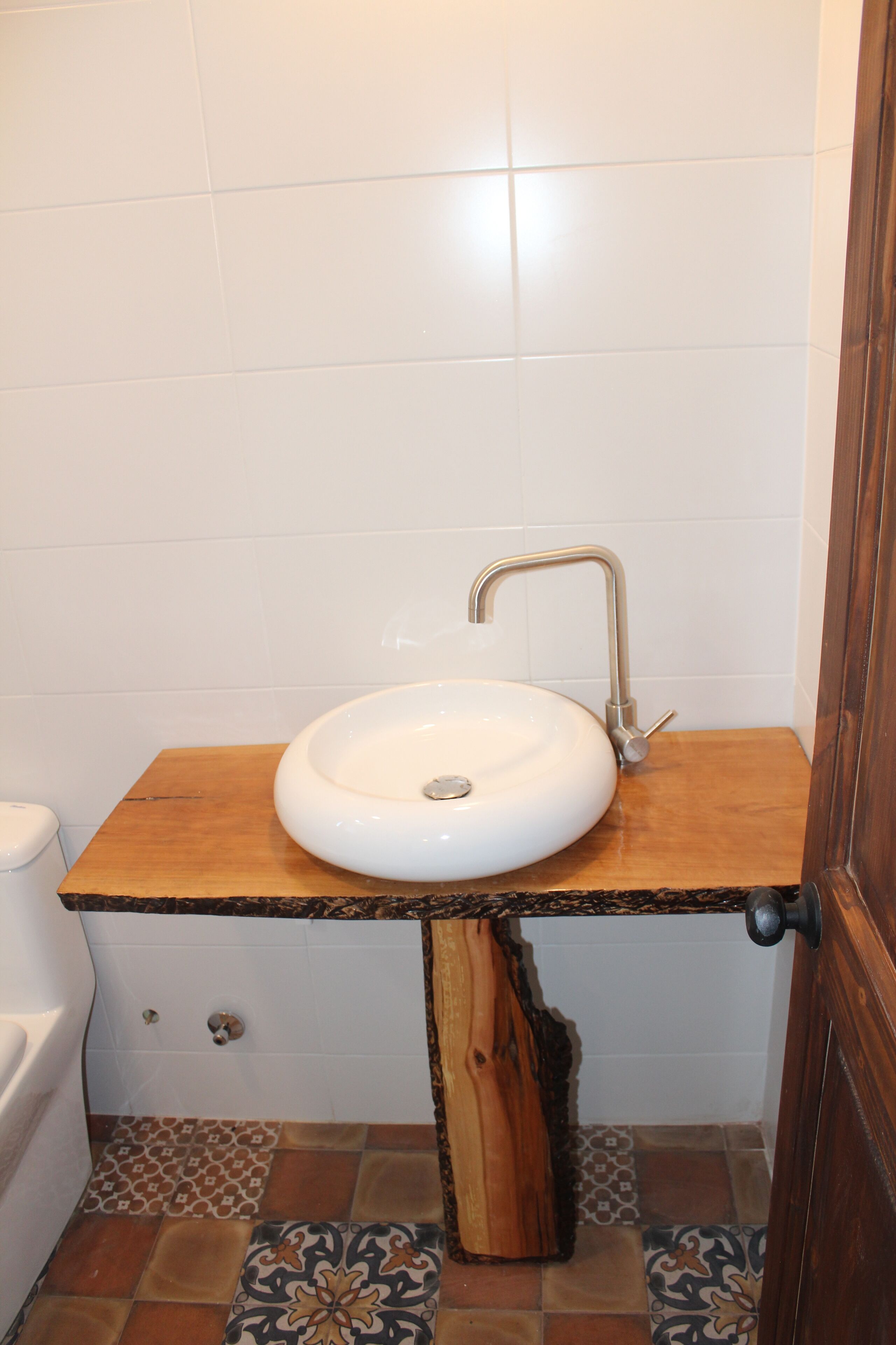 A bathroom with a wooden vanity, white sink, and patterned floor tiles.