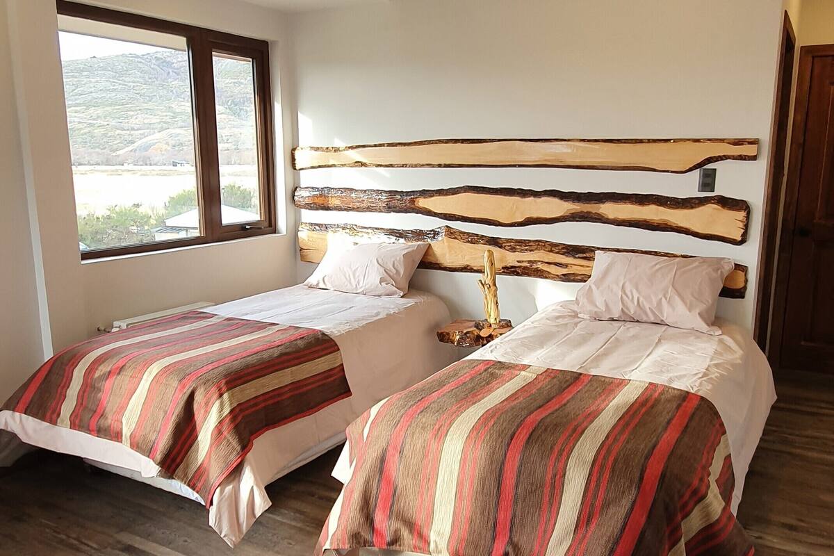 Ein Schlafzimmer mit zwei Betten, Holz-Kopfteilen und einem großen Fenster.