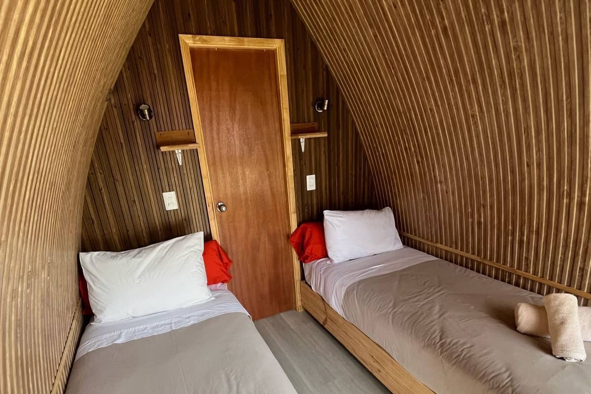 Ein gemütliches Schlafzimmer im Dachgeschoss mit zwei Betten, Holzwänden und einer Holztür.