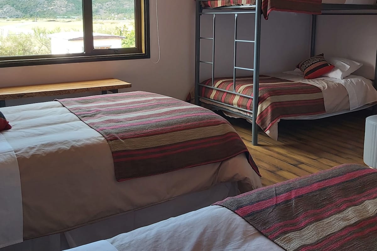 Ein Schlafsaalzimmer mit Etagenbetten, einem Fenster mit Blick auf eine hügelige Landschaft und einer Holzbank.