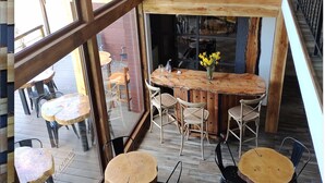 Een restaurantinterieur met houten tafels en stoelen, grote ramen en een zichtbaar buitenterrein.