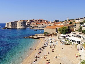 A coastal town with a historic fortification, a sandy beach with sun loungers, and a clear blue sea. - Topfloor Comfortable Luxury Apartment With Private Balcony,free Garage and Wi-fi (Dubrovnik)