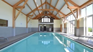 Ein überdachter Pool mit Holzbalken, Fliesenboden und großen Fenstern.