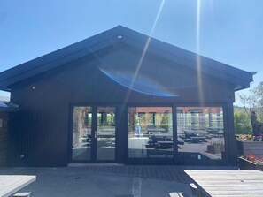 A modern building with large glass doors, a flat roof, and a paved area with benches. - Holiday Home in Rendeux With Pool & Sauna (Rendeux)