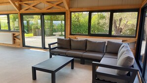 Ein moderner, offener Wohnbereich mit einer Sofagarnitur und einem Couchtisch, große Fenster mit Blick auf Grünflächen, und eine Holzbalkendecke.
