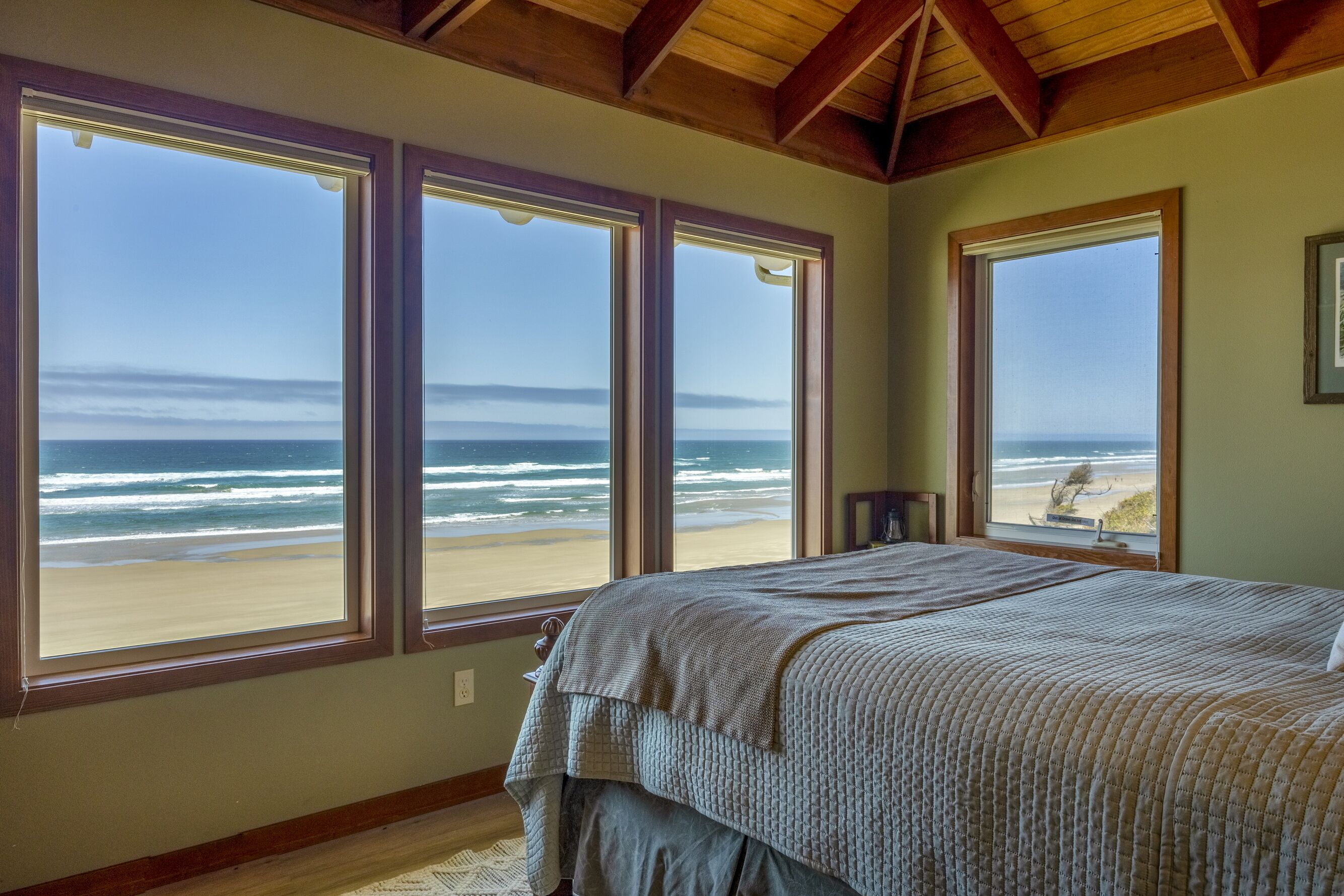 Une chambre à coucher avec un grand lit et trois fenêtres donnant sur la plage et l’océan.