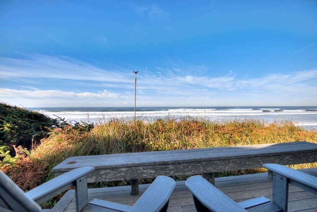 Una panchina di legno con vista su una spiaggia, le onde, un cielo sereno e una veletta.