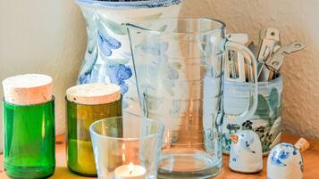 Verschiedene Glasbehälter, darunter eine grüne Flasche, ein transparenter Kerzenhalter und ein dekorativer Krug mit Besteck.