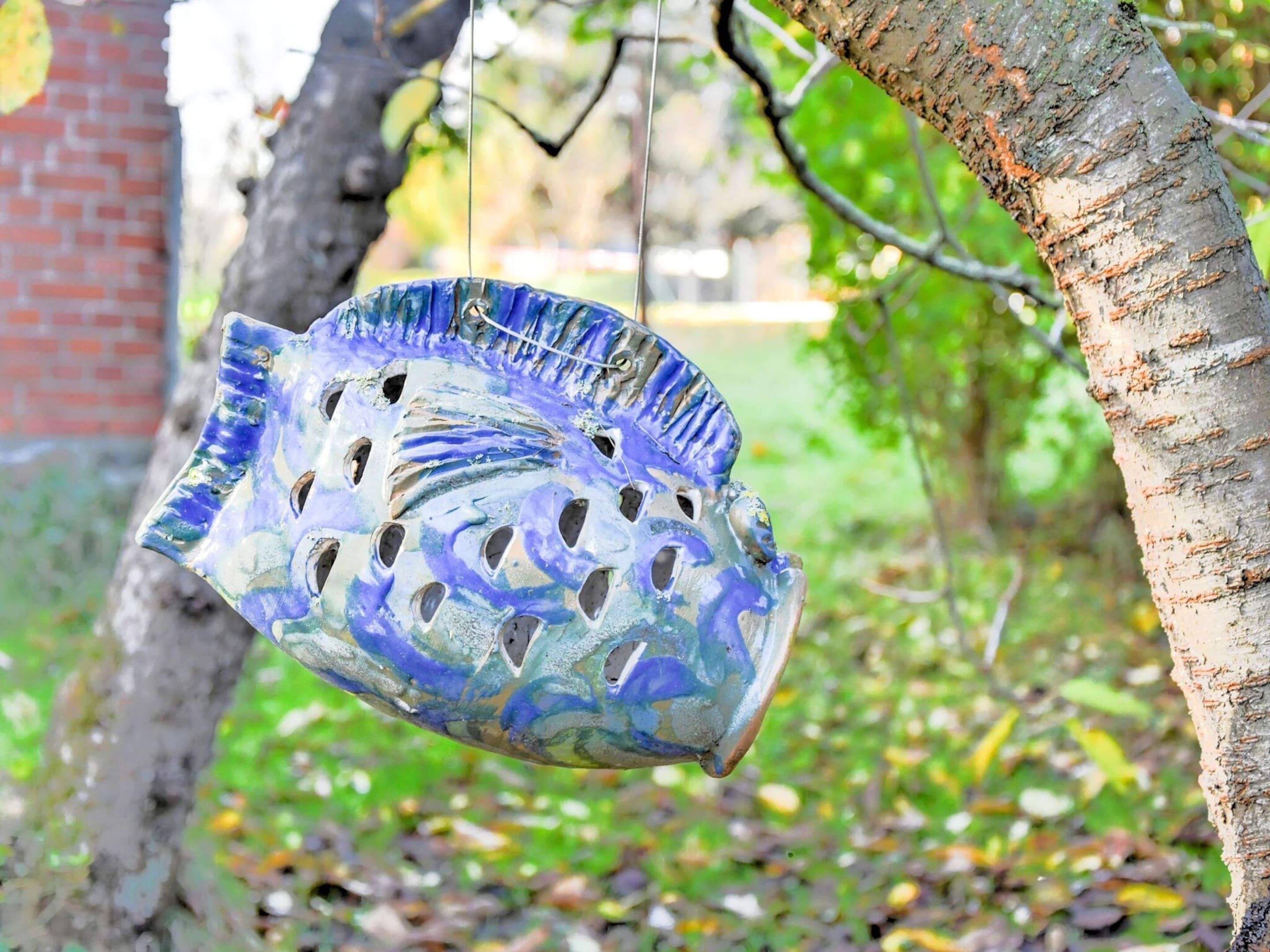 Ein Vogelbad, blau und weiß gestaltet, hängt an einem Baum.