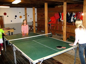 A ping pong table in a room with wooden walls and a foosball table.