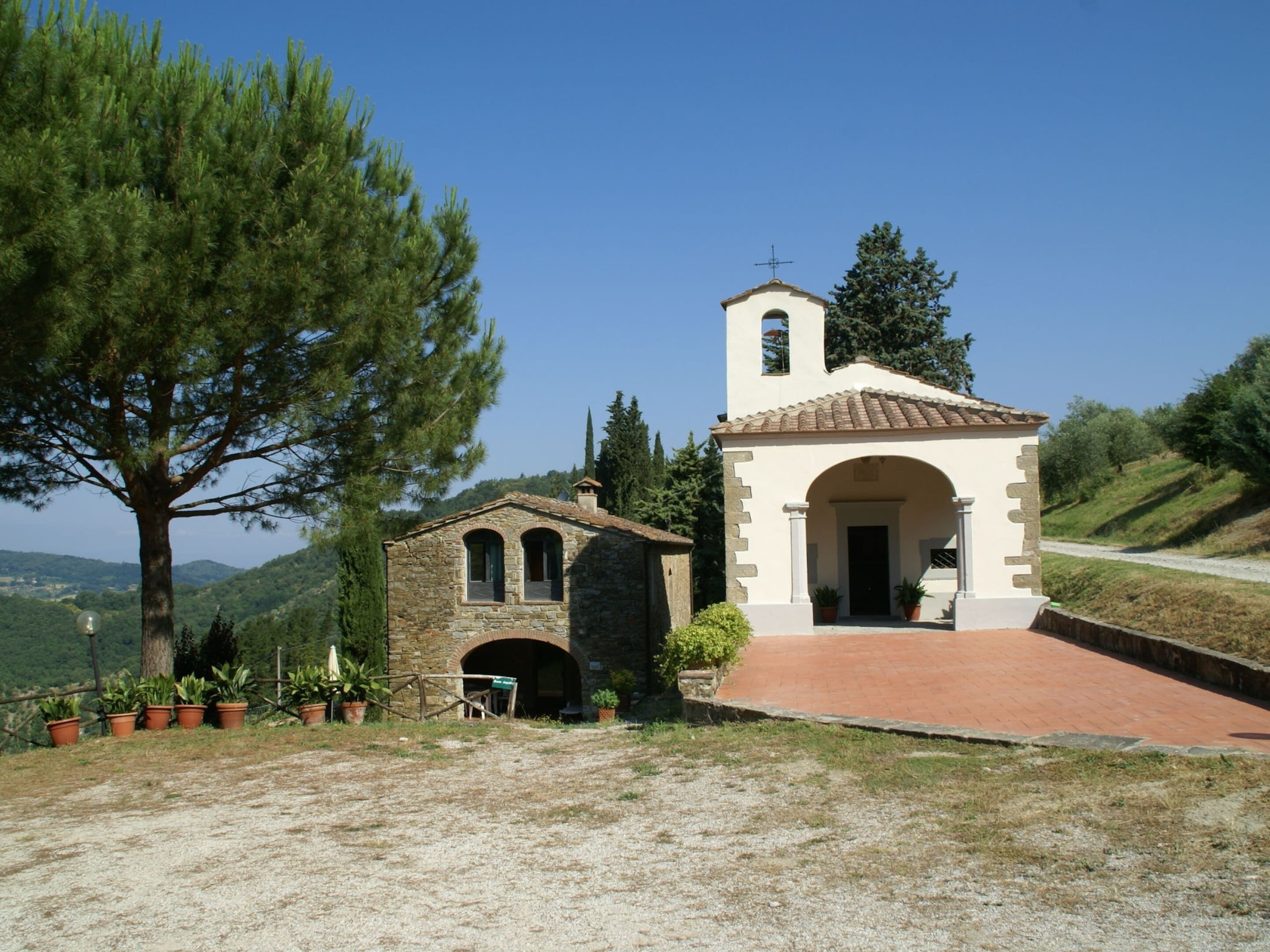 A small stone church with a bell tower, surrounded by trees and a gravel path.