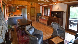 A cozy cabin interior with a wooden dining table, wicker chairs, a kitchen area, and a large window. - Pretty Cottage Ardennes near Valley of Lesse & Semois (Gedinne)