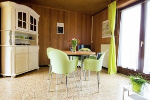 A room with a wooden paneled wall, a white cabinet with glass doors, a round table with chairs, and a window with curtains. - Peaceful Garden Hideaway (Froidchapelle)