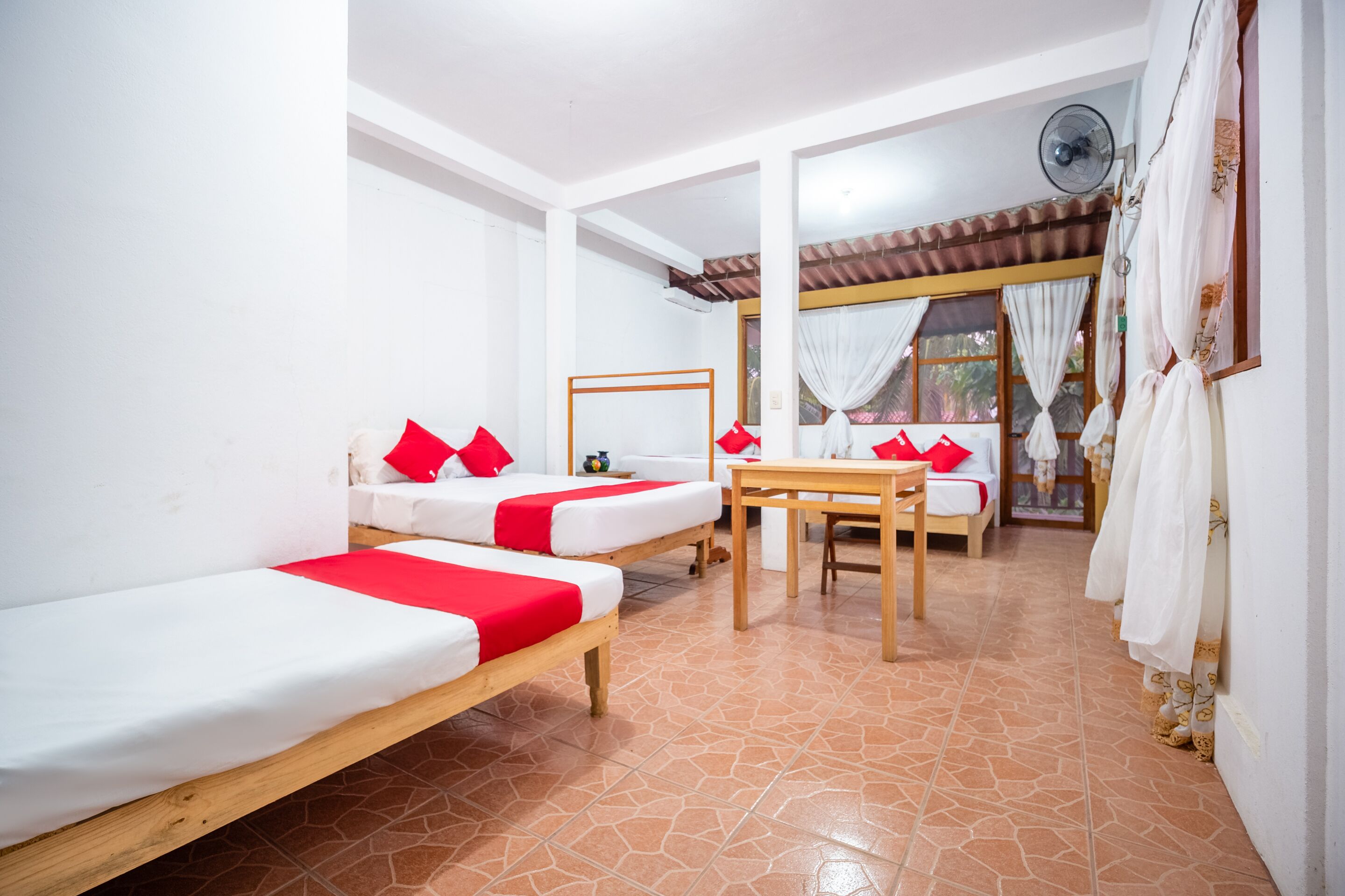 A room with two beds, a table, and a fan.