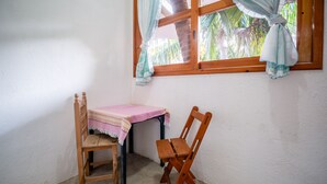 A small room with a wooden table and two chairs, a window with curtains, and a view of palm trees. - OYO Cabañas Abril, Mazunte (Santa María Tonameca)