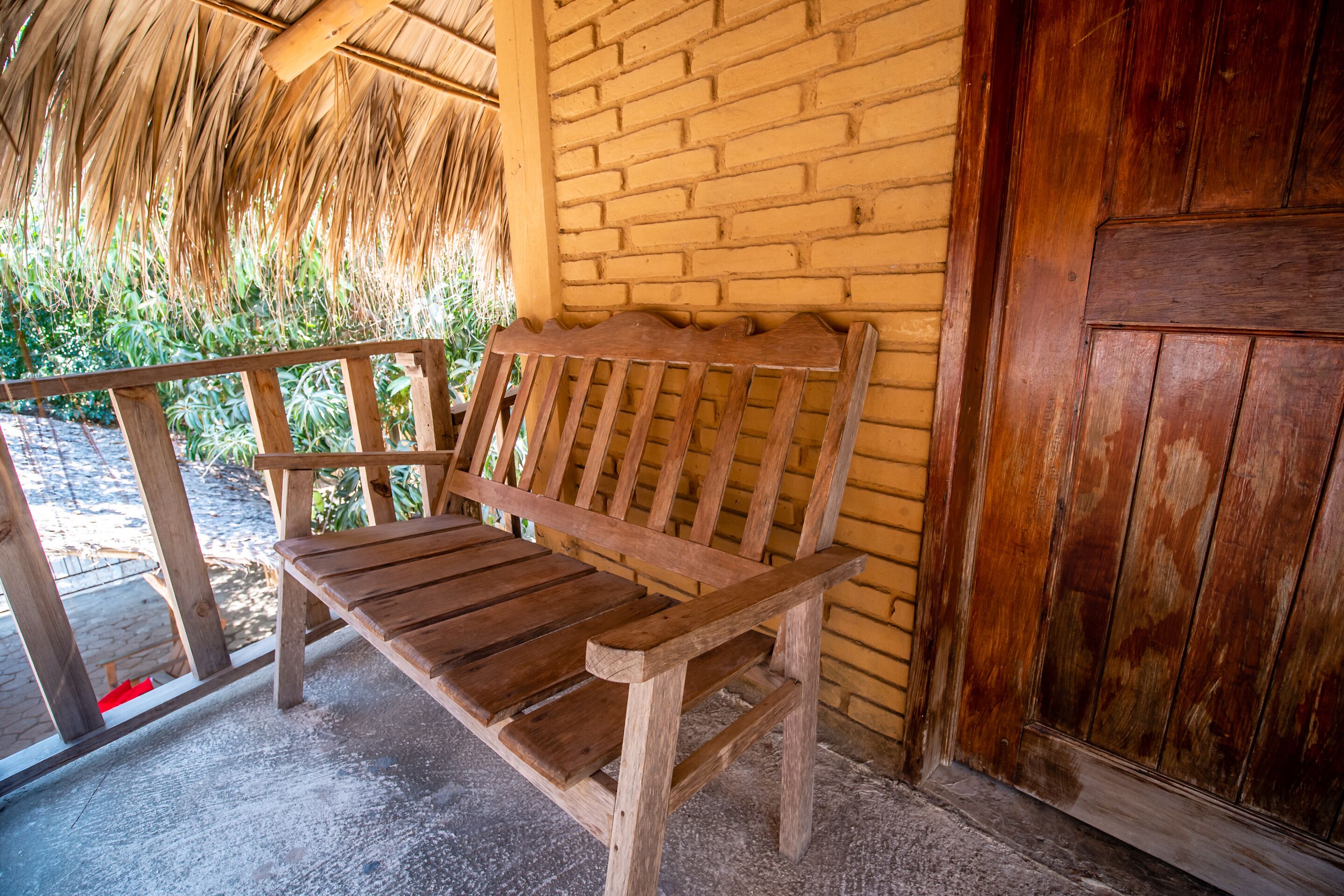 A wooden bench outside a building with a brick wall and a wooden door.