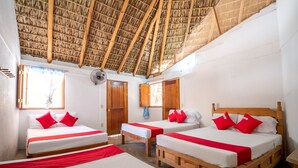 A room with three wooden beds, each with white bedding and red accents, under a thatched roof. - OYO Cabañas Abril, Mazunte (Santa María Tonameca)